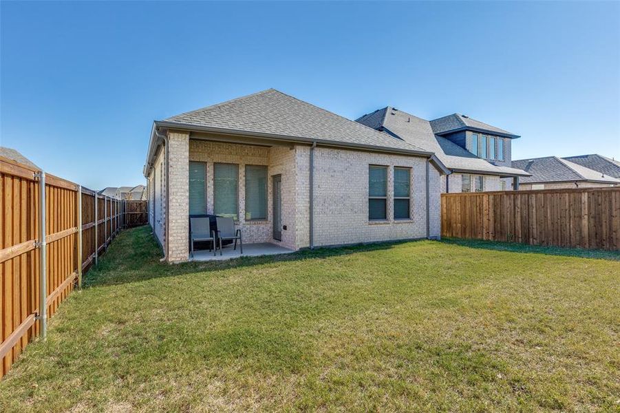 Rear view of property featuring brick siding, roof with shingles, a patio, and a fenced backyard