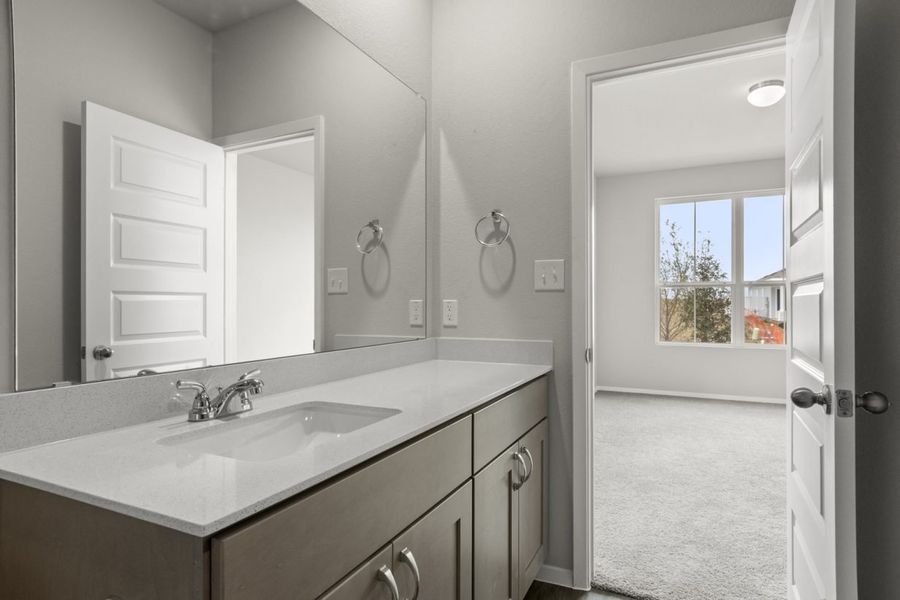 Image of primary bathroom with mirror and white top vanity connected to primary bedroom Image of primary bathroom with mirror and white top vanity connected to primary bedroom