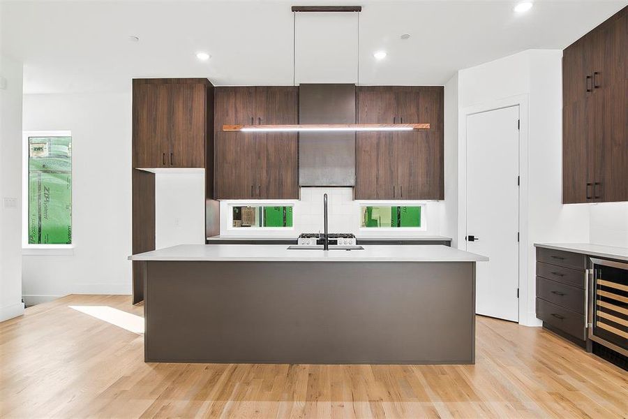 Kitchen featuring dark brown cabinetry, light hardwood floors, wine cooler, and a kitchen island with sink