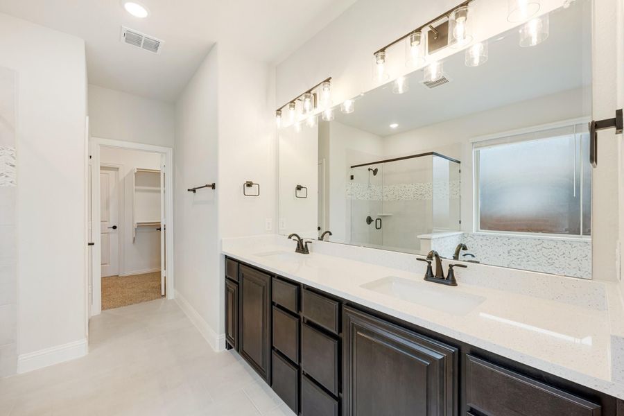 Master bathroom with double vanity, dark cabinets, white countertops, large mirror, and glass shower enclosure