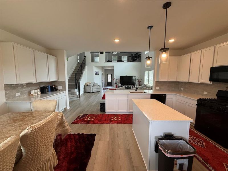 Open-concept kitchen featuring an island with a light-toned countertop, white cabinetry, a neutral backsplash, and wood-finish flooring
