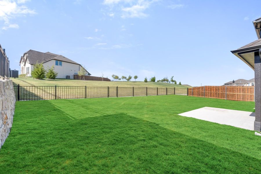 Spacious backyard with green lawn, concrete pad, black iron fence, and wood privacy fence panel
