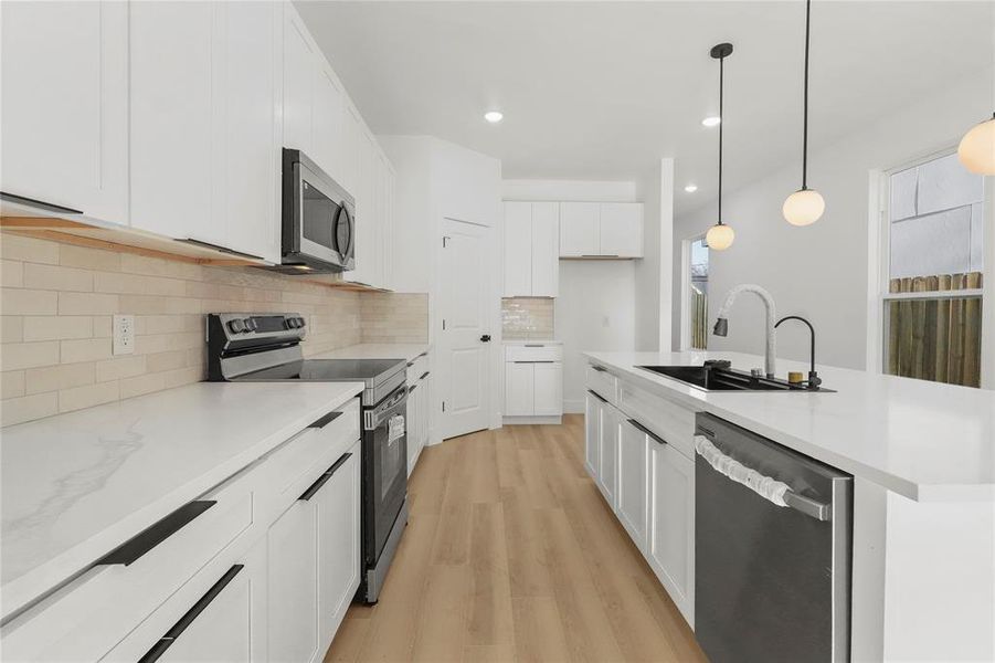 Kitchen with stainless steel appliances, white cabinets, light wood-type flooring, an island with sink, and backsplash