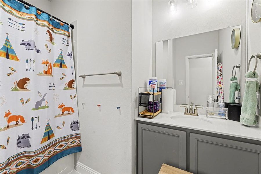 Bathroom featuring a vanity with a white countertop and gray cabinetry, a rectangular mirror, and a shower area