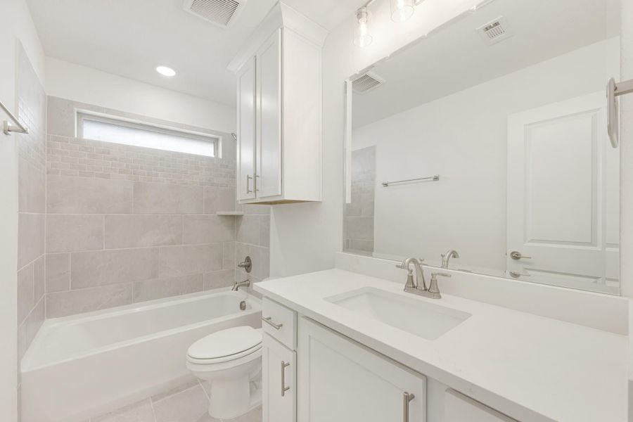 Bathroom with white vanity, quartz countertop, tiled tub surround, and toilet