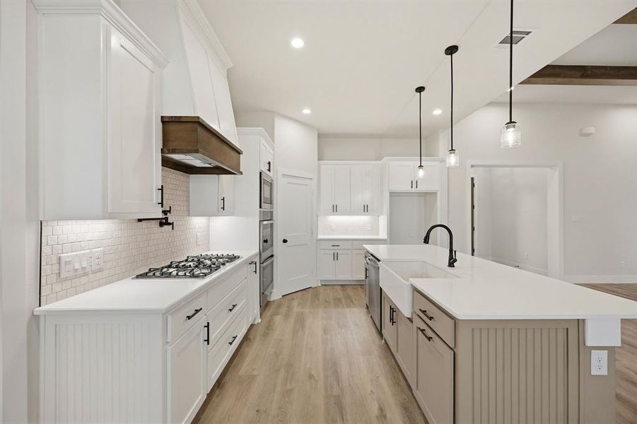 Contemporary kitchen featuring white cabinetry, light wood-finish flooring, a kitchen island with an integrated farmhouse sink, and stainless steel built-in appliances