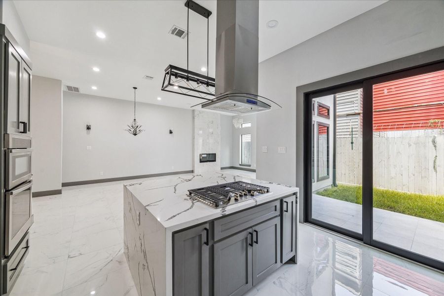 Sliding glass doors open to the patio, showcasing a kitchen anchored by a spacious island with built-in cooktop and a modern hood vent. Double ovens, sleek cabinetry, and clean finishes combine convenience with style. Sliding glass doors open to the patio, showcasing a kitchen anchored by a spacious island with built-in cooktop and a modern hood vent. Double ovens, sleek cabinetry, and clean finishes combine convenience with style.