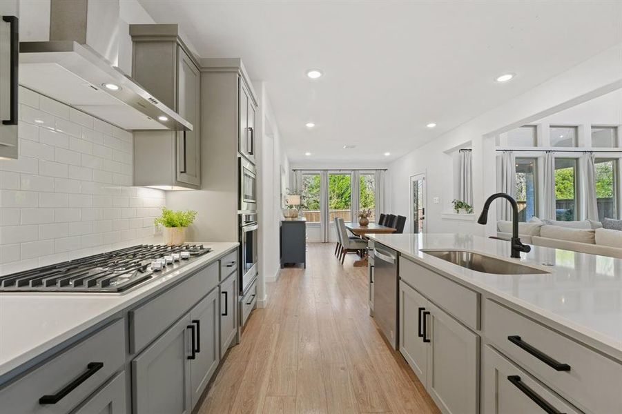 Kitchen featuring wall chimney range hood, light wood-type flooring, gray cabinets, recessed lighting, and tasteful backsplash