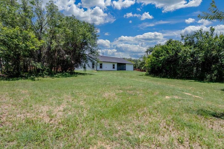 Expansive rear yard featuring natural grass and mature perimeter trees