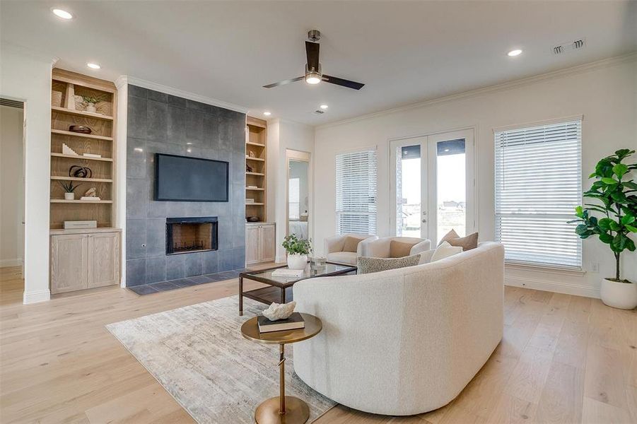 Living room featuring a tile fireplace, ceiling fan, light hardwood / wood-style flooring, and built in features