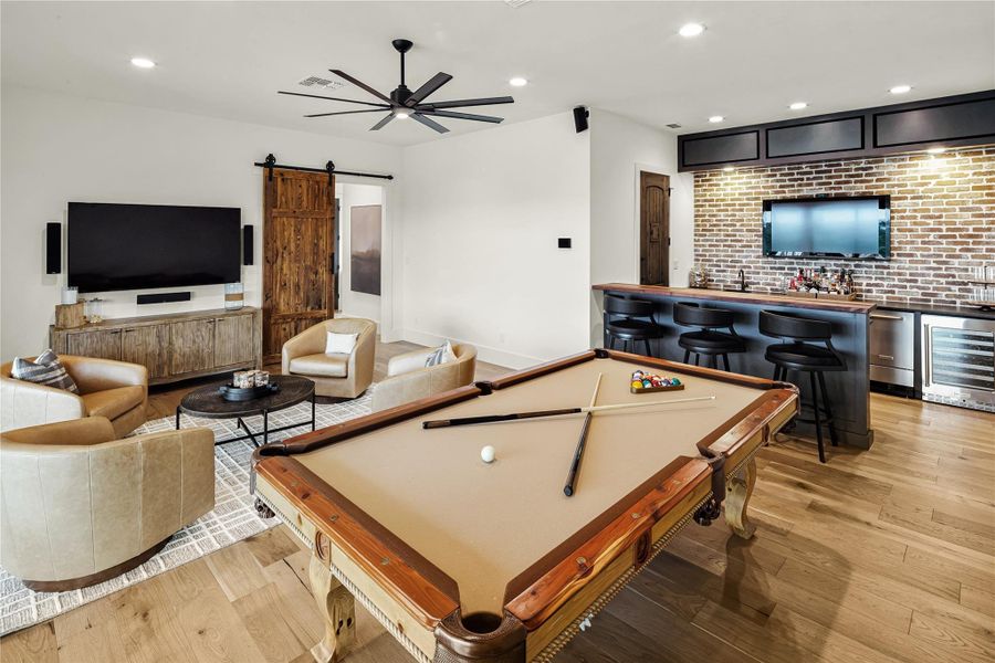 Playroom featuring a barn door, bar area, light hardwood / wood-style flooring, brick wall, and beverage cooler