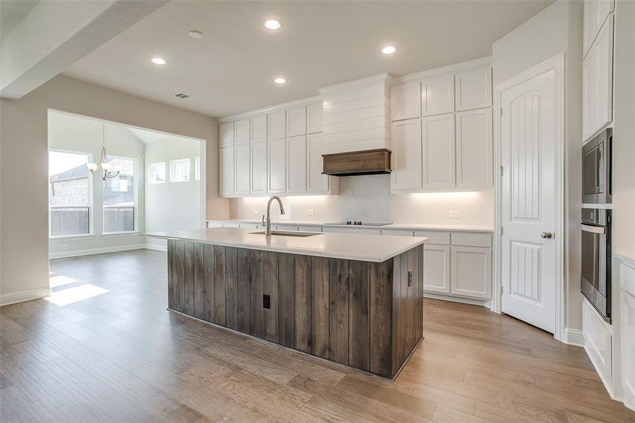 Kitchen with stainless steel appliances, a center island with sink, sink, light wood-type flooring, and white cabinets