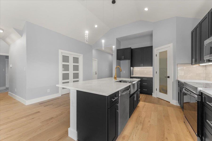 Kitchen with vaulted ceiling, dark cabinets, decorative backsplash, stainless steel appliances, and an island with sink Kitchen with vaulted ceiling, dark cabinets, decorative backsplash, stainless steel appliances, and an island with sink