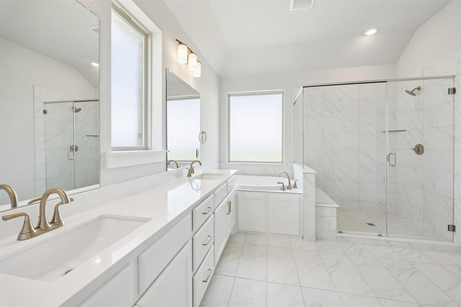 Full bathroom with vaulted ceiling, a shower stall, a garden tub, double vanity, and light marble finish flooring
