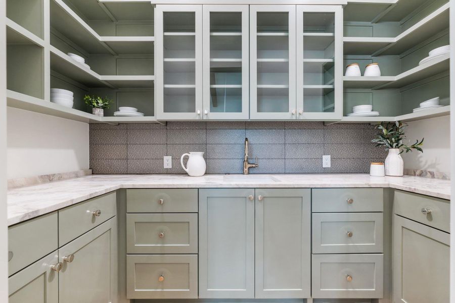 Kitchen with open shelves, light stone counters, tasteful backsplash, and green cabinetry Kitchen with open shelves, light stone counters, tasteful backsplash, and green cabinetry