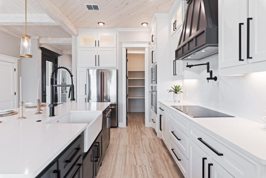Kitchen with black electric cooktop, exhaust hood, a wooden ceiling with exposed beams, white cabinetry, and light countertops Kitchen with black electric cooktop, exhaust hood, a wooden ceiling with exposed beams, white cabinetry, and light countertops
