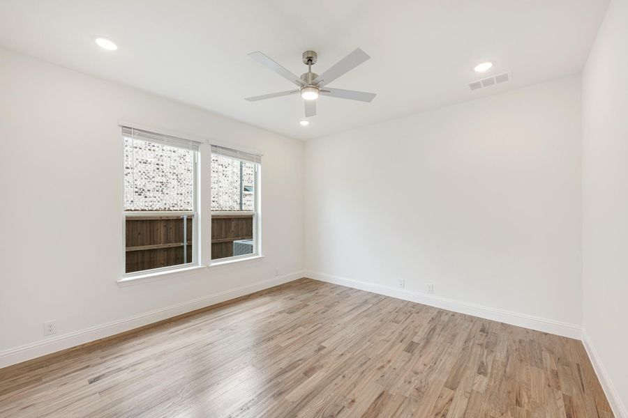 Empty bedroom with hardwood floors, ceiling fan, and two windows with backyard view Empty bedroom with hardwood floors, ceiling fan, and two windows with backyard view