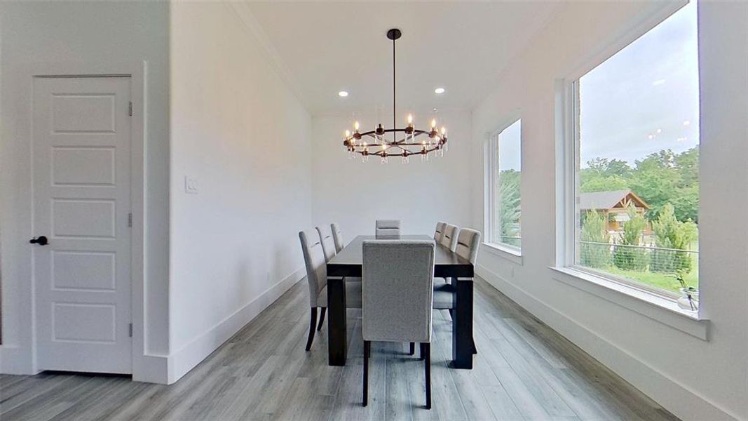 Spacious room featuring multiple large windows, wood-finish flooring, recessed lighting, and a modern chandelier Spacious room featuring multiple large windows, wood-finish flooring, recessed lighting, and a modern chandelier