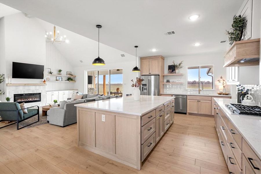 Kitchen featuring stainless steel appliances, light brown cabinets, light hardwood / wood-style floors, a kitchen island, and a tiled fireplace