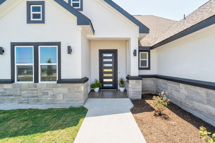 View of exterior entry with stucco siding, stone siding, and roof with shingles View of exterior entry with stucco siding, stone siding, and roof with shingles
