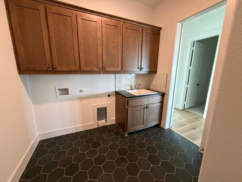 Washroom with electric dryer hookup, hookup for a washing machine, cabinet space, gas dryer hookup, and dark tile patterned flooring