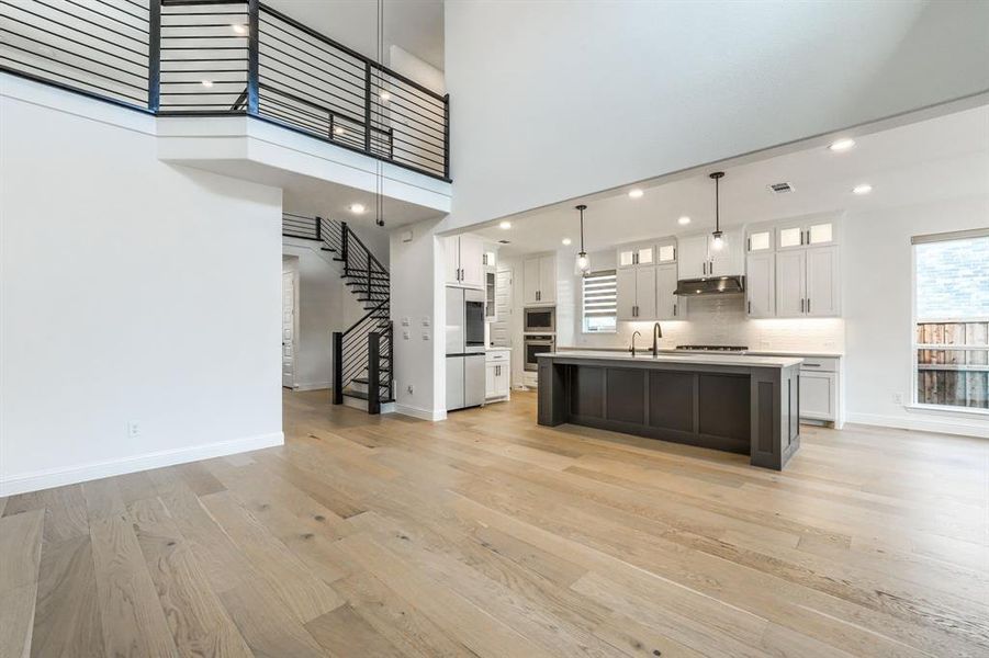 Kitchen with light wood finished floors, under cabinet range hood, light countertops, white cabinets, and stainless steel appliances