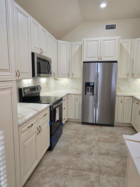 Kitchen with stainless steel appliances, lofted ceiling, tasteful backsplash, light stone counters, and white cabinetry Kitchen with stainless steel appliances, lofted ceiling, tasteful backsplash, light stone counters, and white cabinetry