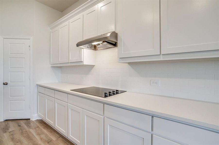 Kitchen featuring range hood, backsplash, black electric cooktop, white cabinets, and light wood-type flooring