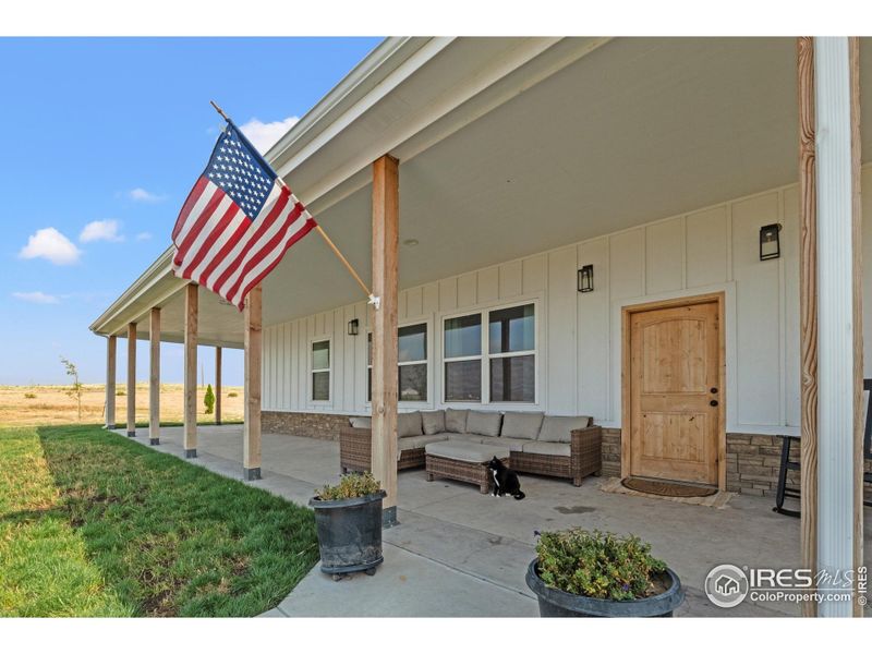 Welcoming front porch with a classic wood entry door. The covered wrap-around design provides shade and charm, perfect for relaxing mornings or evening gatherings.
