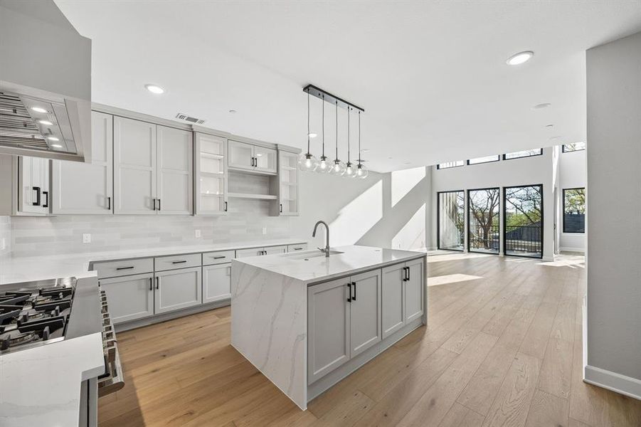 Kitchen with light stone countertops, stainless steel range with gas stovetop, an island with sink, open floor plan, and light wood-type flooring Kitchen with light stone countertops, stainless steel range with gas stovetop, an island with sink, open floor plan, and light wood-type flooring