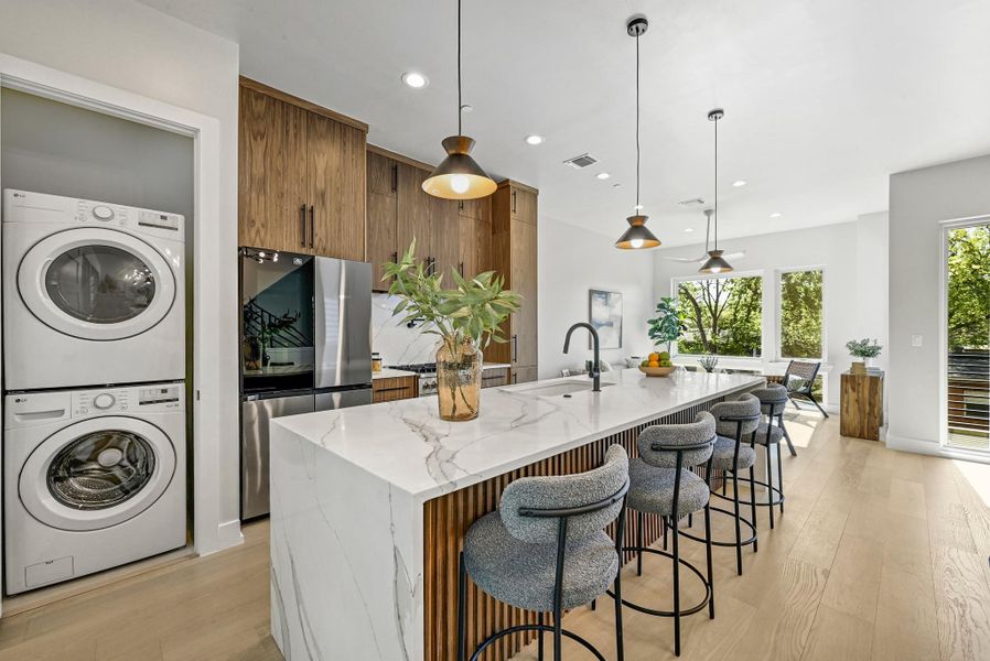 Kitchen featuring custom wood cabinets, quartz waterfall countertop with breakfast bar area, and high end stainless steel appliances. (This is Unit #2 - each Unit has the same layout, however a few differing details such as light fixtures, custom cabinet/backsplash/tile colors)