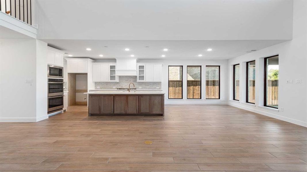 Kitchen featuring an island with sink, light hardwood / wood-style flooring, stainless steel appliances, backsplash, and white cabinetry