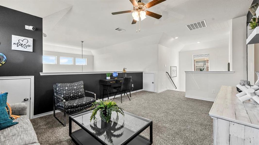 Spacious upper-level loft featuring textured carpeting, vaulted ceilings, and a ceiling fan with integrated lighting
