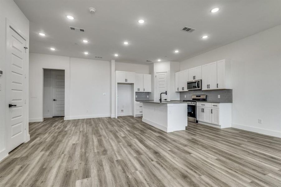 Kitchen featuring white cabinets, light hardwood / wood-style floors, a kitchen island with sink, and appliances with stainless steel finishes