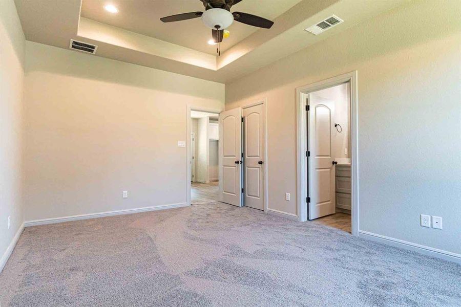 Unfurnished bedroom featuring light colored carpet, a raised ceiling, a ceiling fan, connected bathroom, and recessed lighting