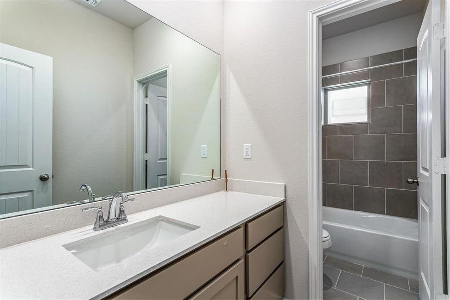 The guest bathroom features a sleek vanity with a modern countertop, offering both style and convenience. The room also includes a shower-tub combination with elegant tile work, making it perfect for guests or family members to refresh and unwind. **This image is from another Saratoga Home - Mockingbird floorplan.**