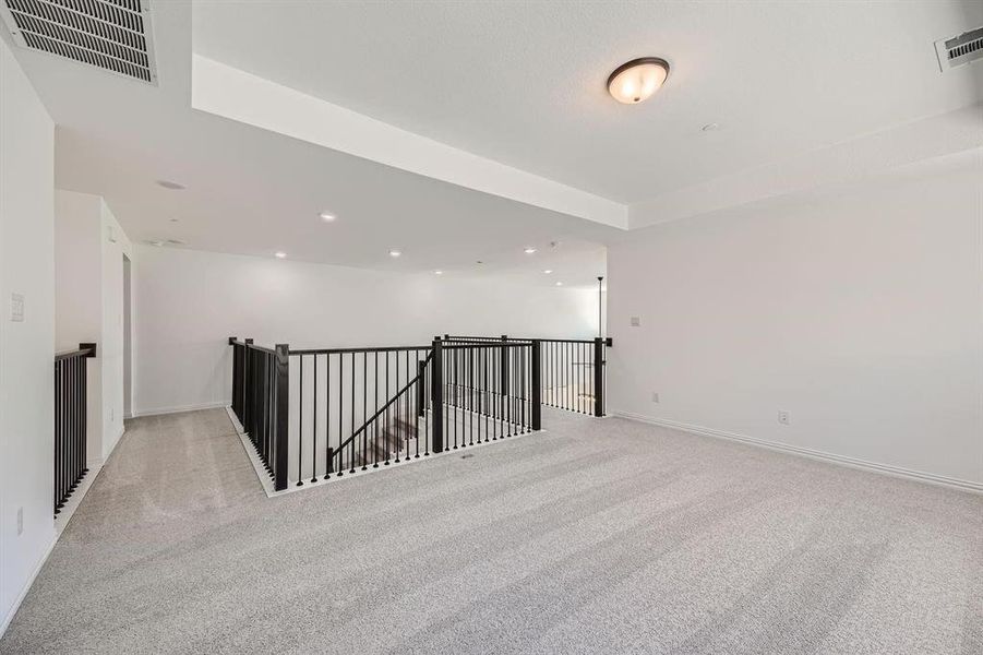 Spacious open landing area featuring light-toned carpeting, white walls, and a modern black metal and wood banister Spacious open landing area featuring light-toned carpeting, white walls, and a modern black metal and wood banister