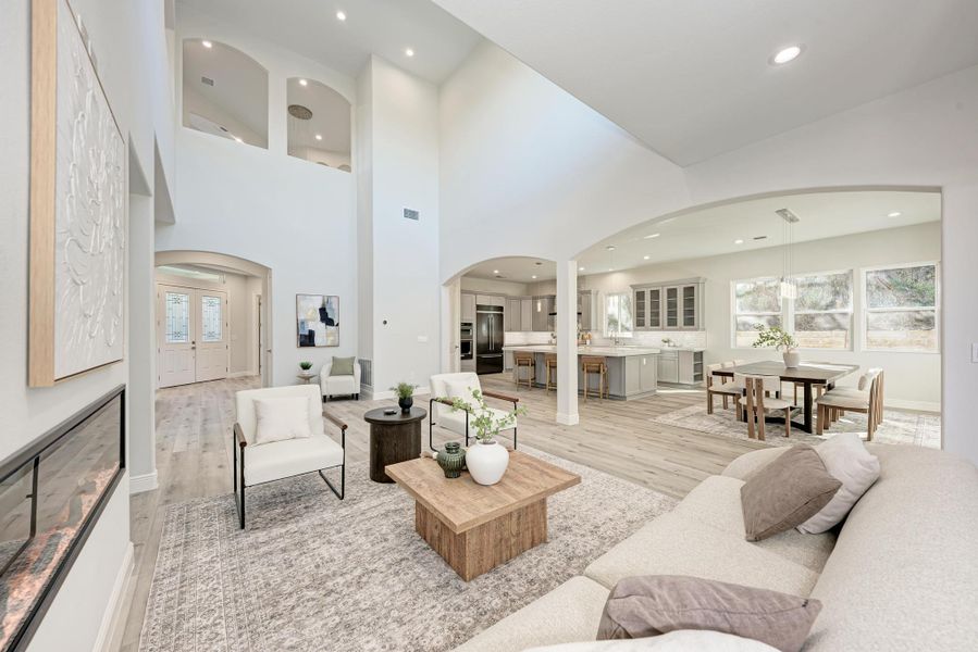 Living room featuring arched walkways, light wood-style flooring, recessed lighting, a fireplace, and a towering ceiling