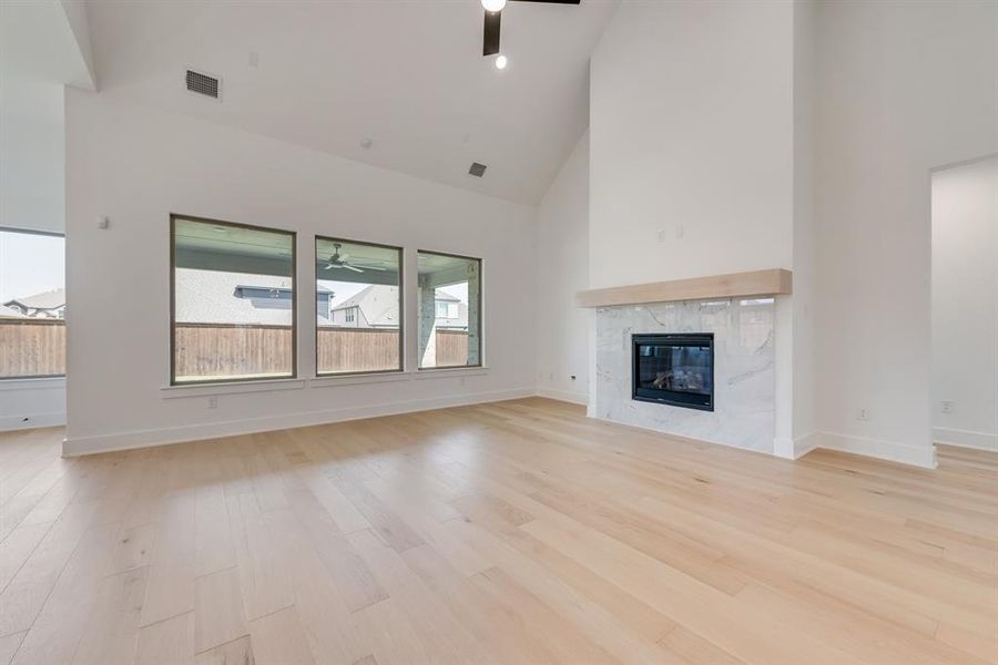 Unfurnished living room with high vaulted ceiling, a ceiling fan, a fireplace, and light wood-type flooring