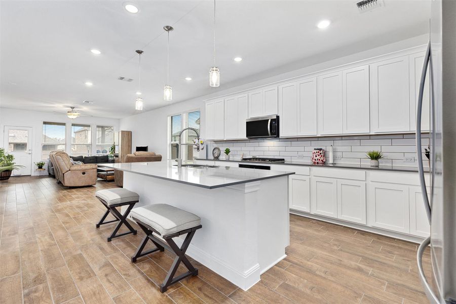 Kitchen with a kitchen breakfast bar, appliances with stainless steel finishes, decorative light fixtures, white cabinetry, and an island with sink