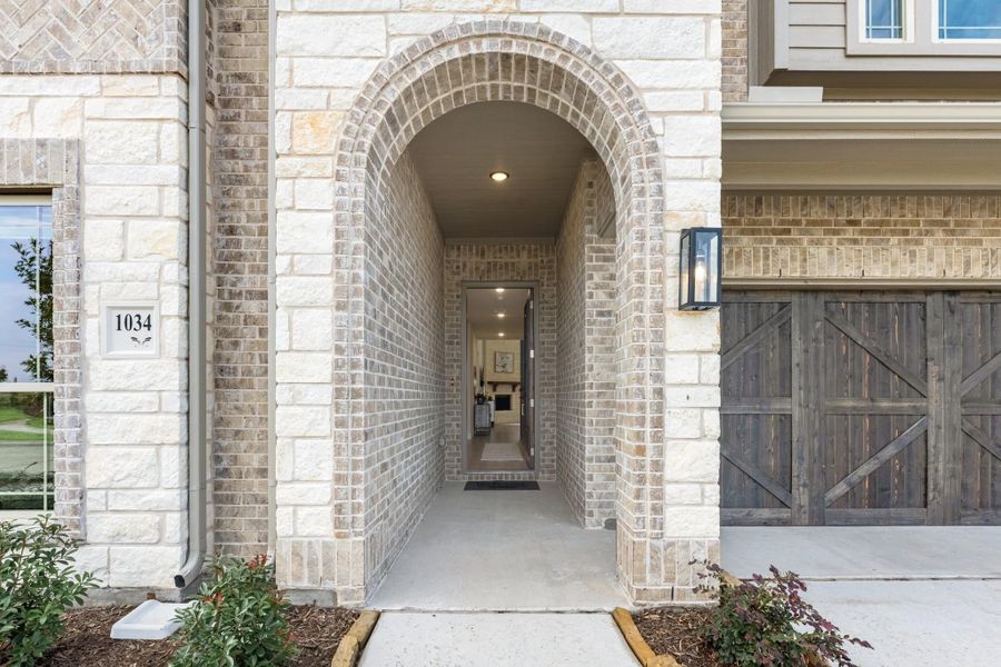 Home entrance with arched brick and stone surround leading to front door, with wood garage door visible to the right. Home entrance with arched brick and stone surround leading to front door, with wood garage door visible to the right.