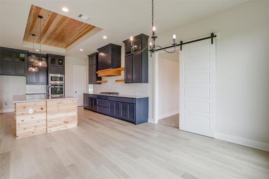 Kitchen with light hardwood / wood-style floors, pendant lighting, a barn door, a raised ceiling, and premium range hood