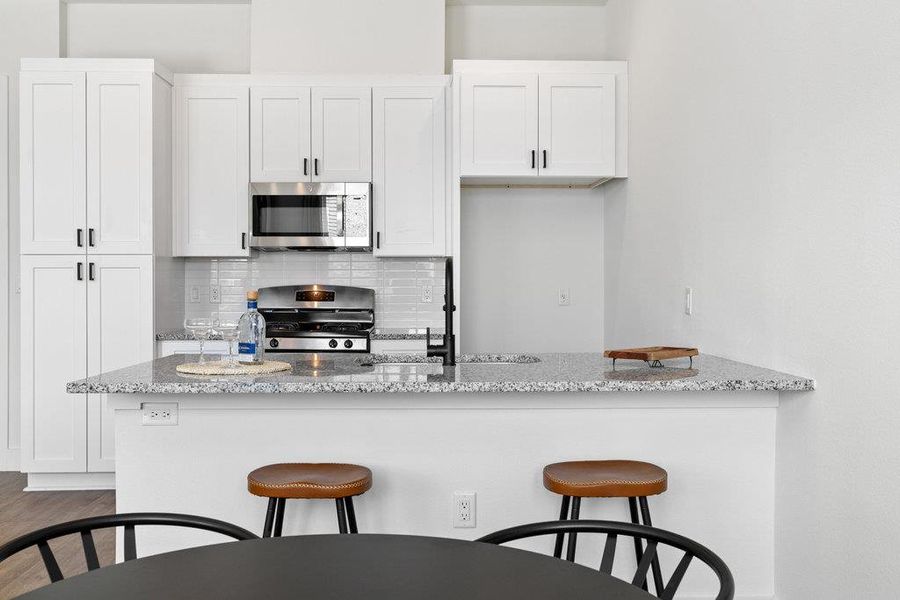 Kitchen with backsplash, a kitchen breakfast bar, white cabinets, and light stone counters