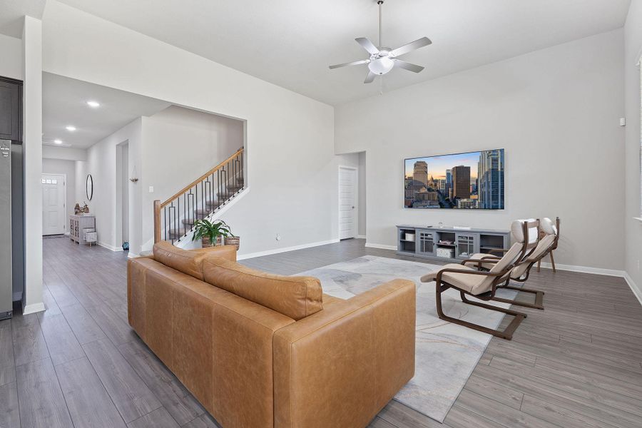 Living room with recessed lighting, light wood finished floors, a ceiling fan, baseboards, and stairs Living room with recessed lighting, light wood finished floors, a ceiling fan, baseboards, and stairs