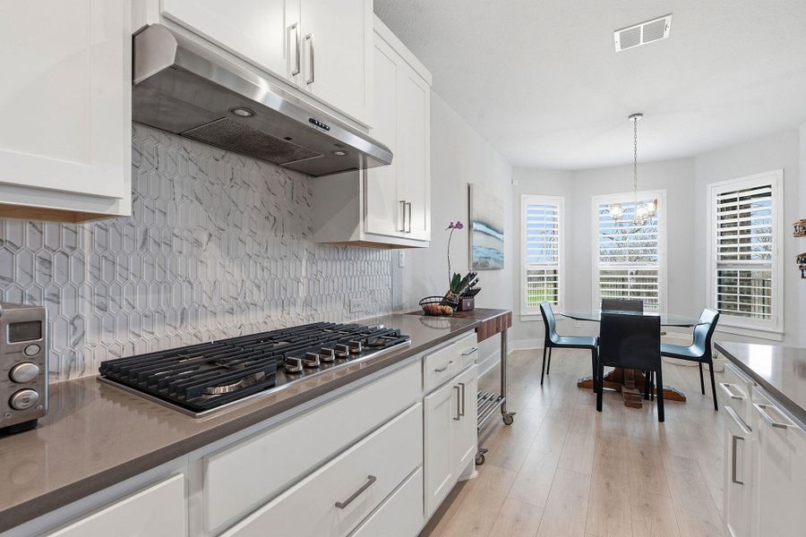 Kitchen featuring white cabinets, stainless steel gas stovetop, light wood-style floors, decorative light fixtures, and dark stone counters