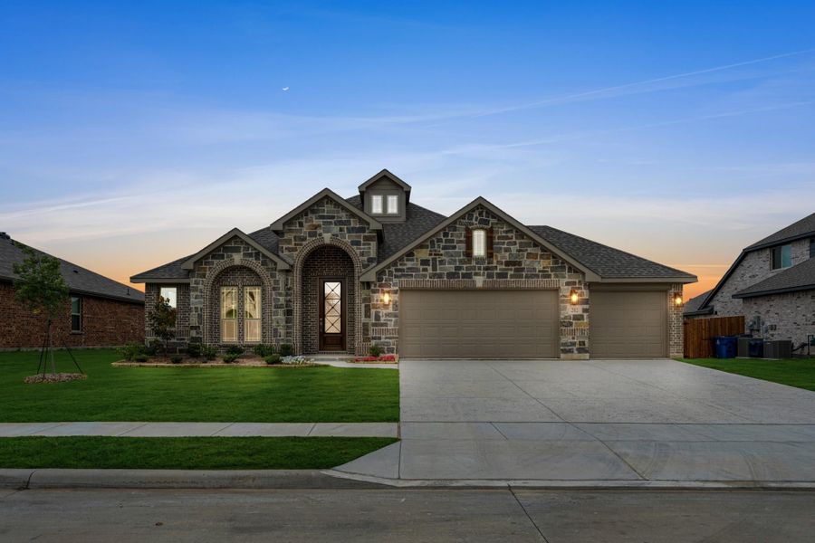 Single-story stone and brick home with arched entry, two-car garage, and green front lawn at dusk