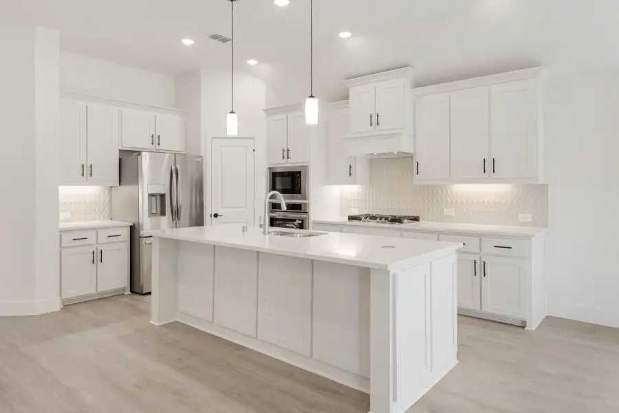 White kitchen with large center island, pendant lights, stainless steel appliances, and light wood floors