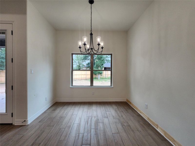 Spacious room featuring wood-finish flooring, a contemporary black chandelier, a large window, and white baseboards