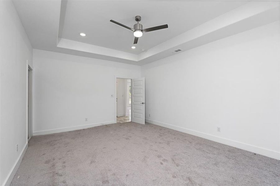 Empty room with carpet flooring, a raised ceiling, and ceiling fan