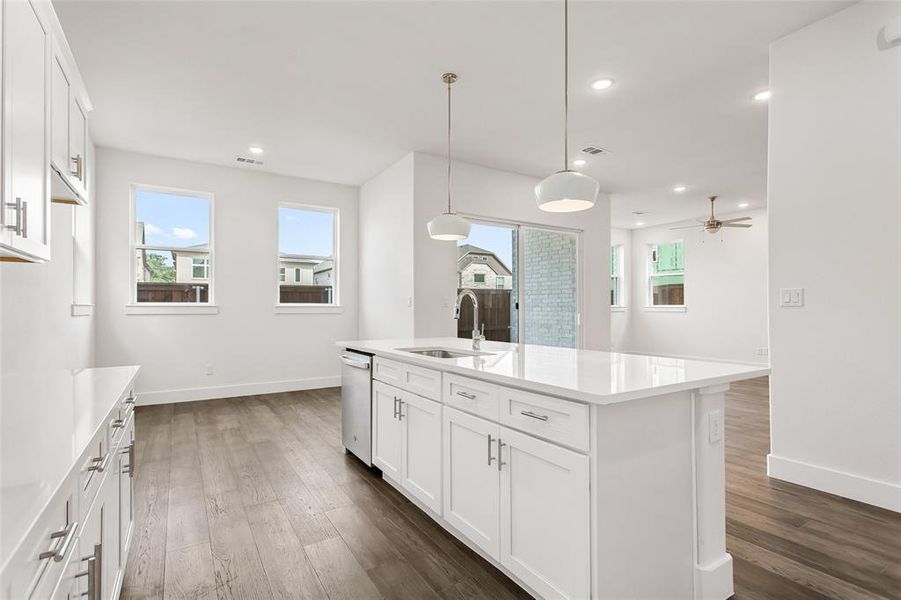 Kitchen with white cabinets, sink, hanging light fixtures, ceiling fan, and an island with sink